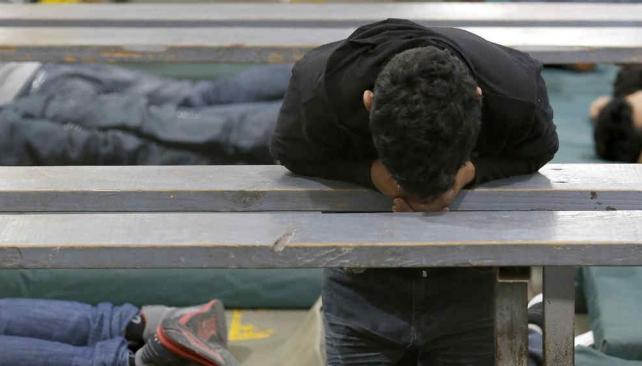 Un joven parece rezar mientras otros duermen y muchos más pasan las horas a la espera de una resolución de sus casos (AP).